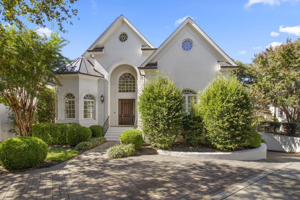 Ivory brick home with twin gables, round windows and an arched entry in West Raleigh, NC, photographed by Lightwell Haus